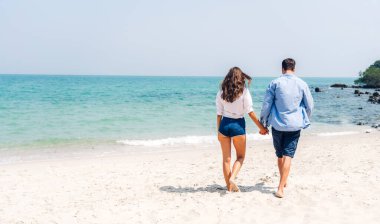 Romantik aşıklar genç mutlu çift deniz kenarında el ele tutuşup tropik sahillerde eğleniyorlar. Yaz tatilleri ve seyahatler.
