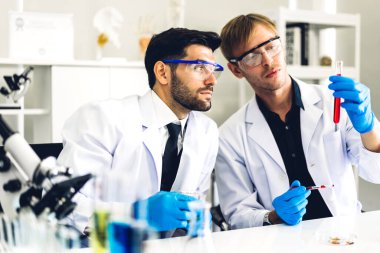 Profesyonel iki bilim adamı test tüpünde sıvı analiz ederken ve karıştırırken kimyasal bir deney yapıyor. Genç bilim adamı laboratuvarda cam üzerine kimyasal örnekler bırakıyor.