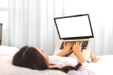 Kadın evdeki yatağın üzerinde beyaz boş ekranlı dizüstü bilgisayar teknolojisi kullanıyor. İletişim ve teknoloji kavramı.