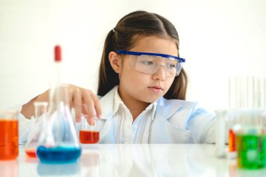 Şirin küçük kız öğrenci araştırma yapmayı ve kimyasal deney yapmayı öğrenirken fen bilimleri sınıfında sıvıyı analiz edip karıştırıyor. Eğitim ve bilim konsepti.