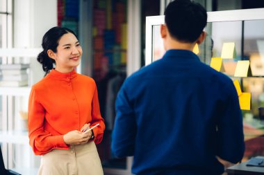 Gündelik yaratıcı mutlu iki gülümseme Asyalı iş adamları strateji analizi ve beyin fırtınası planlıyorlar. Çıkartma yapıştırmaları yapıştırıyorlar ve modern ofisin cam tahtasında başlangıç projesi için fikir paylaşıyorlar.