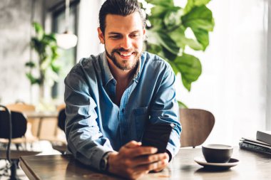 Yakışıklı hippi kahve ile dijital akıllı telefon kullanarak rahatlıyor ve kafeteryada ve restoranda ekran daktilo mesajlarına bakıyor, online ve sosyal medyada oyun oynuyor.