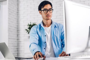Sofaa 'da otururken dizüstü bilgisayar izleme teknolojisine bakan yakışıklı Asyalı iş adamı. Evde klavyede çalışan ve daktilo yazan genç yaratıcı iş arkadaşları.