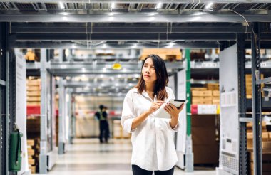 Gülümseyen Asyalı yönetici kadın portresi ayakta duruyor ve malzeme ve gereçleri depoda kontrol etmek için tablet bilgisayardan ayrıntılı talimat veriyor. Lojistik ve iş ihracatı