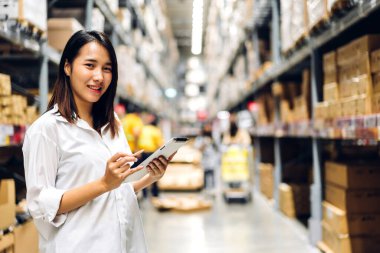 Gülümseyen Asyalı yönetici kadın portresi ayakta duruyor ve malzeme ve gereçleri depoda kontrol etmek için tablet bilgisayardan ayrıntılı talimat veriyor. Lojistik ve iş ihracatı