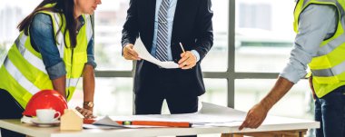 İnşaat alanındaki masanın üzerinde tasarım ve inşaat araçlarıyla çalışan miğferli kargo ustabaşıları.