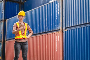 Miğferli profesyonel mühendis kargo kadını ayakta çalışıyor ve tablet kullanarak stokları yükleme için konteynıra koyuyor. Lojistik ve iş ihracatı