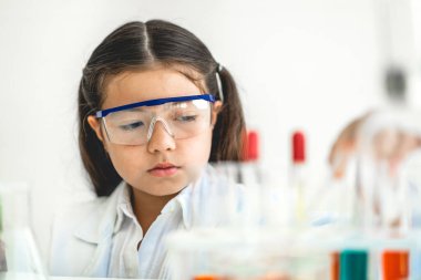 Tatlı küçük kız öğrenci araştırma öğreniyor ve kimyasal bir deney yapıyor aynı zamanda fen bilimleri sınıfında sıvıyı analiz edip karıştırıyor. Eğitim ve bilim konsepti.