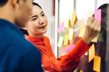 Gündelik yaratıcı mutlu iki gülümseme Asyalı iş adamları strateji analizi ve beyin fırtınası planlıyorlar. Çıkartma yapıştırmaları yapıştırıyorlar ve modern ofisin cam tahtasında başlangıç projesi için fikir paylaşıyorlar.