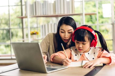 Anne ve Asyalı küçük kız öğreniyor ve dizüstü bilgisayara bakıyor ev ödevi yapıyor çevrimiçi eğitim e-öğrenme sistemiyle bilgi öğreniyor. Evde öğretmenle çocuk video konferansı