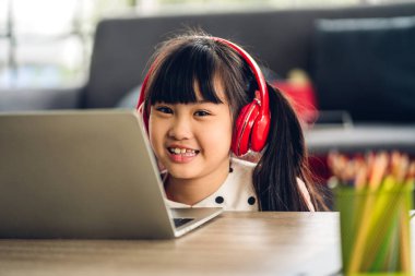 Okul çocuğu küçük kız öğreniyor ve dizüstü bilgisayara bakıyor ev ödevi yapıyor çevrimiçi eğitim sistemi ile bilgi öğreniyor. Evde öğretmenle çocuk video konferansı
