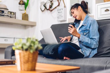 Genç gülümseyen Asyalı kadın dizüstü bilgisayar kullanıyor ve evdeki iş arkadaşlarıyla çevrimiçi toplantı yapıyor. Genç yaratıcı kız, ev konseptinden iş ekibiyle video konuşması yapıyor.