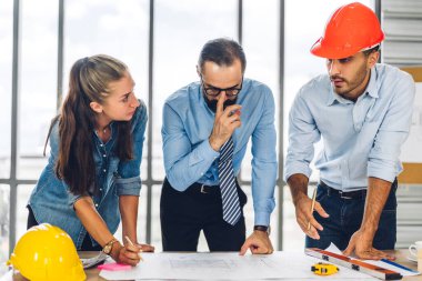 İnşaat alanındaki masanın üzerinde tasarım ve inşaat araçlarıyla çalışan miğferli kargo ustabaşıları.