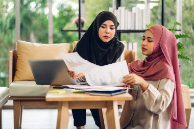 Genç, gülümseyen mutlu Asyalı Müslüman kadın evde dizüstü bilgisayar, tablet çalışma ve video konferans kullanarak rahatlıyor. Ev konseptinden iş.