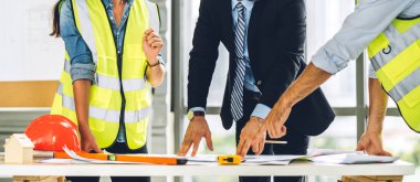 İnşaat alanındaki masanın üzerinde tasarım ve inşaat araçlarıyla çalışan miğferli kargo ustabaşıları.