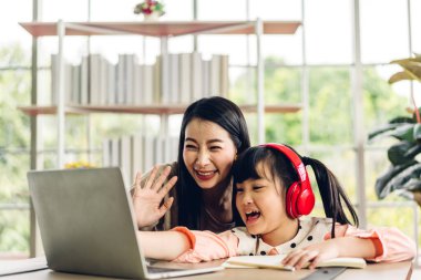 Anne ve Asyalı küçük kız öğreniyor ve dizüstü bilgisayara bakıyor ev ödevi yapıyor çevrimiçi eğitim e-öğrenme sistemiyle bilgi öğreniyor. Evde öğretmenle çocuk video konferansı