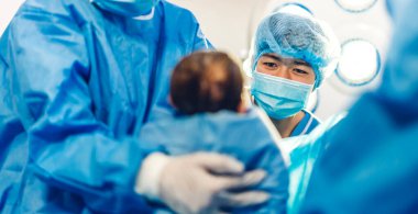 Profesyonel anestezi uzmanı doktor tıbbi ekip ve asistan bebek sezaryeni yapıyor ve bebeği modern hastane ameliyathanesinde doğum ekipmanıyla doğuruyor.