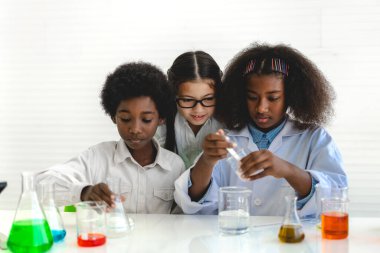 Okuldaki deney laboratuarında test tüpünde sıvı karıştırıp analiz ederken araştırma yapmayı ve kimyasal deney yapmayı öğrenen bir grup küçük tatlı öğrenci. Eğitim.