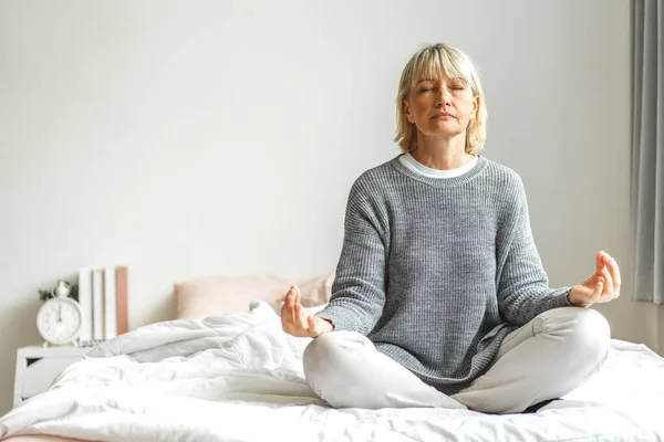 Portrait of elderly woman sitting and do yoga.Attractive senior woman fitness training workout exercise on bed at home