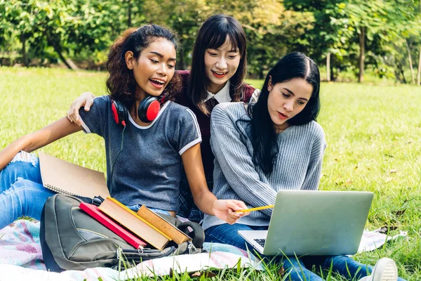 一群微笑的国际学生或青少年坐在一起 用笔记本电脑和书本一起在大学的公园里做作业 教育和友谊的概念 — 图库照片
