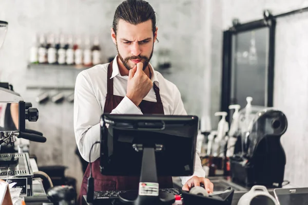 Yakışıklı sakallı baristanın portresi. Küçük işletme sahibi. Kafenin arkasında bilgisayarla çalışıyor.