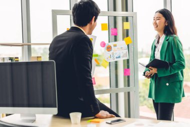 Gündelik yaratıcı mutlu iki gülümseme Asyalı iş adamları strateji analizi ve beyin fırtınası planlıyorlar. Çıkartma yapıştırmaları yapıştırıp modern ofisin cam tahtasında başlangıç projesi için fikir paylaşıyorlar.