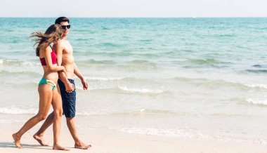 Romantik aşıklar genç mutlu çift deniz kenarında el ele yürüyor ve tropik plajlara metin eklemek için fotokopi çekiliyor. Yaz tatilleri ve seyahatler