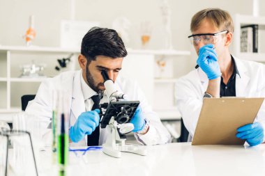 Profesyonel iki bilim adamı test tüpünde sıvı analiz ederken ve karıştırırken kimyasal bir deney yapıyor. Genç bilim adamı laboratuvarda cam üzerine kimyasal örnekler bırakıyor.