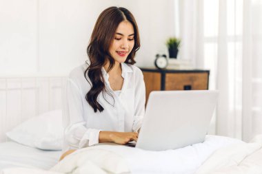 Soğuk bir kış günü yatak odasında dizüstü bilgisayar kullanan genç Asyalı kadın. Sosyal uygulamaları ve çalışmaları kontrol eden kadın. İletişim ve teknoloji kavramı.