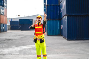 Miğferli profesyonel mühendis konteynır ustabaşı ayakta çalışıyor ve telsiz kullanıyor stokları yükleme için konteynıra koyuyor. Lojistik ve iş ihracatı