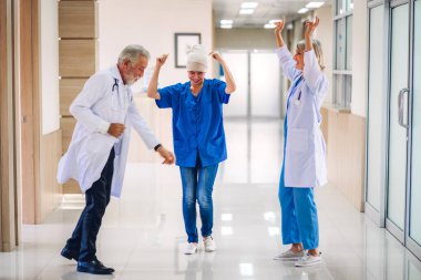 Steteskoplu profesyonel tıp doktoru ekibi hastanede başörtüsü kemoterapi kanseri olan mutlu bir hastayla tartışıyor ve dans ediyor.