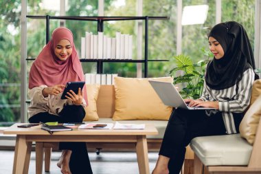 Genç, gülümseyen, mutlu, Asyalı Müslüman bir kadın dizüstü bilgisayarını kullanarak rahatlıyor ve evde video konferansı yapıyor. Ev konseptinden çalışma.
