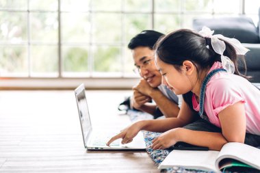 Baba ve Asyalı küçük kız öğreniyor ve dizüstü bilgisayara bakıyor. İnternetten eğitim öğrenim sistemiyle bilgi öğreniyor. Öğretmenle çocuk video konferansı.