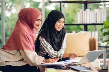 Genç, gülümseyen, mutlu, Asyalı Müslüman bir kadın dizüstü bilgisayarını kullanarak rahatlıyor ve evde video konferansı yapıyor. Ev konseptinden çalışma.