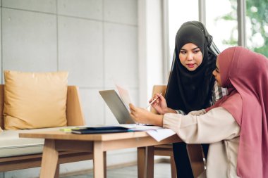 Genç, gülümseyen, mutlu, Asyalı Müslüman bir kadın dizüstü bilgisayarını kullanarak rahatlıyor ve evde video konferansı yapıyor. Ev konseptinden çalışma.