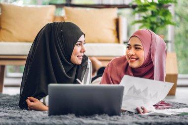 Genç, gülümseyen, mutlu, Asyalı Müslüman bir kadın dizüstü bilgisayarını kullanarak rahatlıyor ve evde video konferansı yapıyor. Ev konseptinden çalışma.