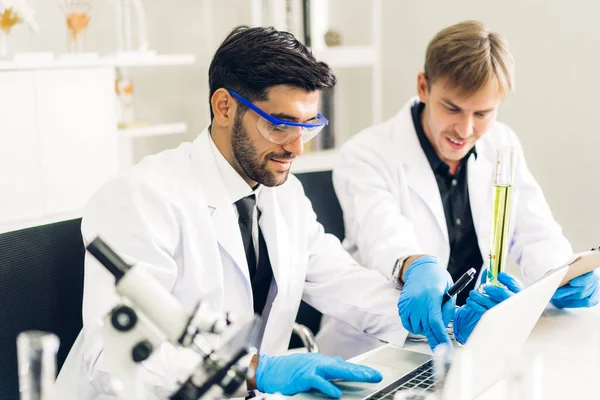 Professional two scientist man research and working doing a chemical experiment while making analyzing and mixing liquid in test tube.Young science man dropping sample chemical on glass at laboratory