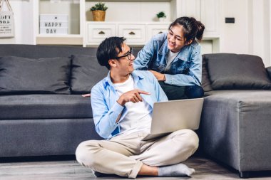 Genç Asyalı çift dizüstü bilgisayarlarını kullanarak rahatlıyor ve birlikte internet sitelerine bakıyorlar. Yaratıcı iş çifti online alışveriş yapıyor ve evde film seyrediyor.