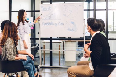 Koronavirüs karantinasında sosyal mesafeli koruyucu maske takan bir grup profesyonel iş sunumu toplantısı. Yaratıcı iş planlaması ve dizüstü bilgisayarlı beyin fırtınası.