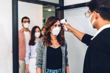 Bir grup profesyonel Asya işi ve ofiste koruyucu maske takarak koronavirüs için karantinada çalışmadan önce vücut ısısını ölçmek için kızılötesi termometre kullanılıyor.