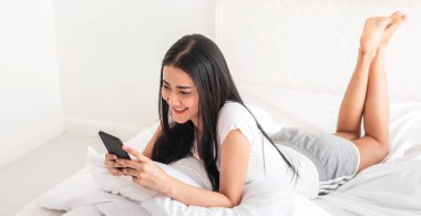 Gülümseyen mutlu Asyalı kadın portresi dijital teknoloji akıllı telefon kullanarak rahatlıyor. Genç Asyalı kız ekranda yazı yazma ve evde oyun oynama ya da sosyal medya oyunlarına bakıyor.