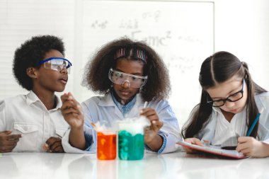 Okuldaki deney laboratuarında test tüpünde sıvı karıştırıp analiz ederken araştırma yapmayı ve kimyasal deney yapmayı öğrenen bir grup küçük tatlı öğrenci. Eğitim.