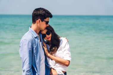 Romantik aşıklar. Genç mutlu çift, tropikal sahilde sarılıp kumsalda durup eğleniyor ve dinleniyorlar. 