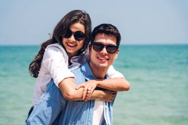 Romantik aşıklar. Genç mutlu çift, tropikal sahilde sarılıp kumsalda durup eğleniyor ve dinleniyorlar. 