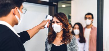 Bir grup profesyonel Asya işi ve ofiste koruyucu maske takarak koronavirüs için karantinada çalışmadan önce vücut ısısını ölçmek için kızılötesi termometre kullanılıyor.