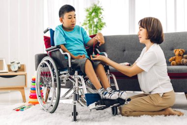 Asyalı fizyoterapistin portresi engelli çocuk sağlığı sorununa rehabilitasyon kliniğinde tekerlekli sandalyede oturarak yardım ve oyun oynayarak yardımcı oluyor.