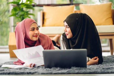 Genç, gülümseyen, mutlu, Asyalı Müslüman bir kadın dizüstü bilgisayarını kullanarak rahatlıyor ve evde video konferansı yapıyor. Ev konseptinden çalışma.