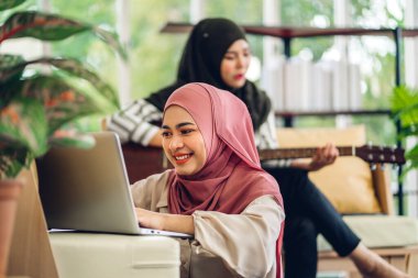 Genç, gülümseyen, mutlu, Asyalı Müslüman bir kadın dizüstü bilgisayarını kullanarak rahatlıyor ve evde video konferansı yapıyor. Ev konseptinden çalışma.