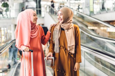 İki genç, güzel, Asyalı Müslüman kadın tesettüre girmiş, alışveriş yapıyor ve moda mağazasında sohbet ederken eğleniyor.