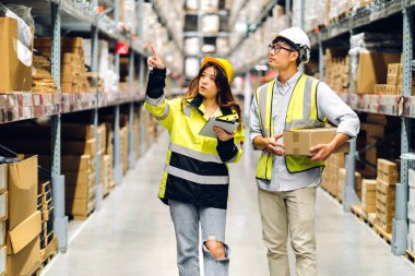 Miğfer takımındaki Asyalı iki mühendis, malzeme ve malzemelerin depo geçmişine sahip raflarda kontrol edilmesi için tablet bilgisayardan talimat verdi. Lojistik ve iş ihracatı